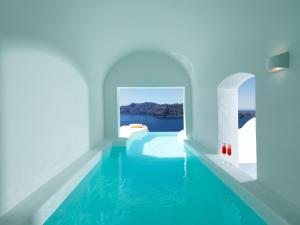 a swimming pool in a room with the ocean in the background at Katikies Santorini - Pelagos House - The Leading Hotels Of The World in Oia
