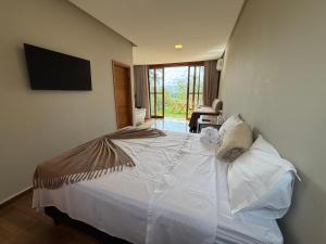 a bedroom with a white bed with a flat screen tv at Pousada Carraro in Delfinópolis
