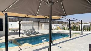 an umbrella over a pool with chairs and a table at Olives Hill Farm in Al Kufayr