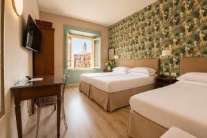 a hotel room with two beds and a desk and a window at Hotel della Vittoria in Ancona