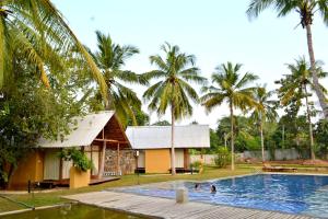 a swimming pool in front of a house with palm trees at Kottawatta Village in Udawalawe