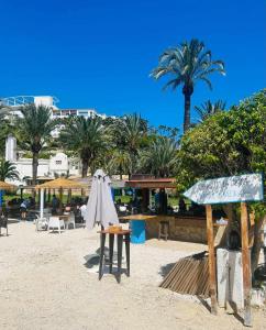 a beach with tables and umbrellas and palm trees at Pequeño estudio frente al mar, piscina y parking in Villajoyosa