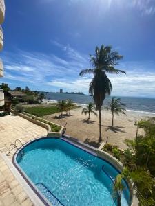 a swimming pool next to a beach with a palm tree at Beach View Palace in Porlamar