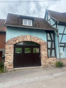 a blue house with a black garage door at La Cabane in Dambach-la-Ville