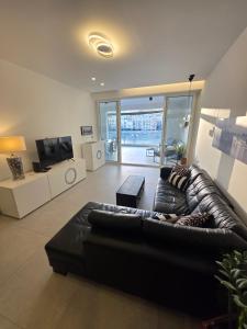 a living room with a black leather couch and a television at Luxury Waterfront 3BR Apartment with Large Terrace in Marsaskala
