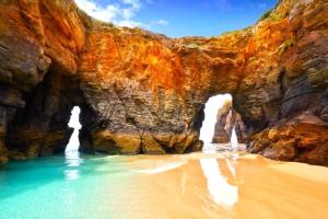 an arch in the rocks on a beach with water at Dúplex 4 dormitorios Playa Foz in Foz