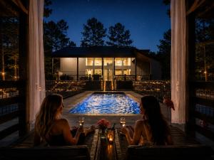 two women sitting on a porch in front of a pool at night at Creek,Pool,Playhouse celebration estate, sleeps 21 in Broken Bow