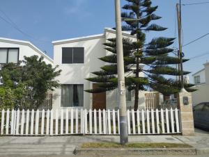 a white fence and a pine tree in front of a house at Casa en condominio in Moche