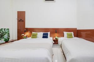 two beds in a room with white sheets and green pillows at Urbanview Darmo Residence Bandung in Bandung