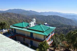 a house with a green roof with mountains in the background at Rudraa Himalayan Retreat in Hawālbāgh