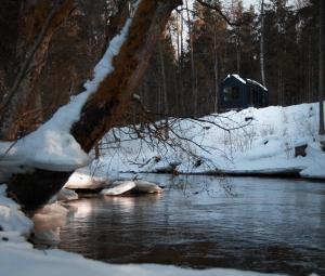 a river with snow and a cabin in the background at refleXions in Kabakelis