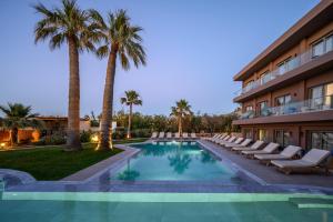 a hotel with a swimming pool with chairs and palm trees at Malia Bay Beach Hotel & Bungalows in Malia
