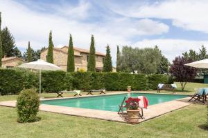 a swimming pool with chairs and umbrellas in a yard at Villa Campriano by VacaVilla in Pienza