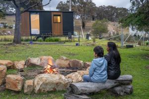 a woman and a child sitting next to a fire at Sparkling Tiny House by Tiny Away in Windeyer