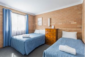 a bedroom with two beds and a brick wall at Emu Beach Chalets in Albany