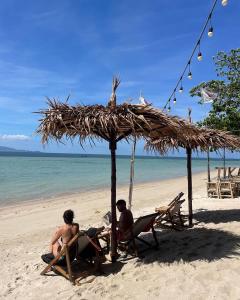 two men sitting in chairs under a straw umbrella on a beach at Tiki Beach Koh Phangan Beach Restaurant Bar and Coworking in Ban Tai