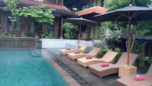 a pool with lounge chairs and umbrellas next to a building at Dewa Bungalows, A Balinese House and Art Gallery in Ubud