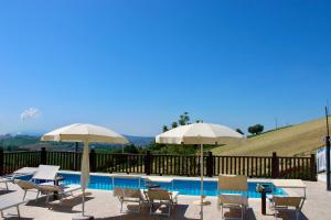 a pool with two umbrellas and chairs and a table at Respiro di Tramonto in Montegranaro
