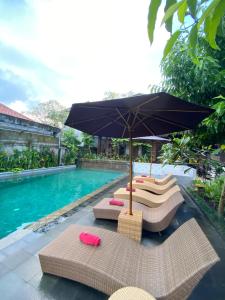 a pool with chairs and an umbrella next to a swimming pool at Dewa Bungalows, A Balinese House and Art Gallery in Ubud