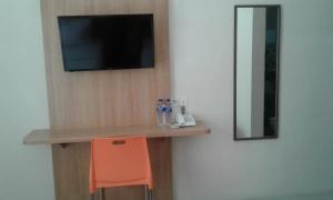 a room with a desk with a television and a orange chair at Hotel Ella Tambolaka in Tambolaka Airport
