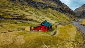 a small red house on a hill next to a river at Saksun Mountain & Beach Cottage in Saksun