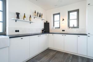 a white kitchen with white cabinets and two windows at Reetidyll am Haff - Haus 2 in Stolpe auf Usedom +15 photos
