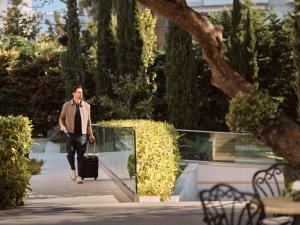 a man walking down a sidewalk with a suitcase at Civitel Attik Rooms & Suites in Athens
