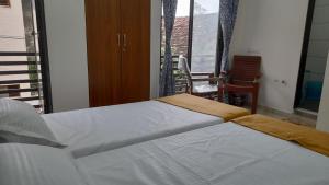 a bedroom with two beds and a window with a chair at Hotel Madhav Shankar in Rajkot