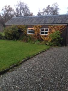 una casa cubierta de hiedra con una entrada de grava en Woodside Cottage Self Catering en Kinbuck