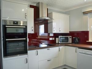a kitchen with white cabinets and black appliances at Tall Pines in Carrbridge