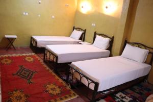 three beds in a room with a red rug at Kol izem in Ksar el Kbir