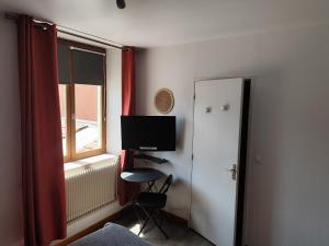 a room with a television and a chair and a window at Hotel de la Place in Loyettes
