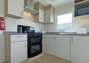 a kitchen with white cabinets and a black oven at The Chase Holiday Park in Addlethorpe