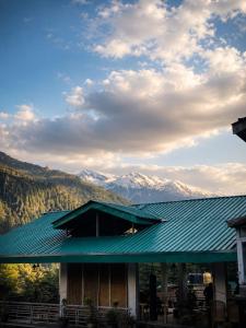 a building with a green roof with mountains in the background at Negi Wooden House in Manāli