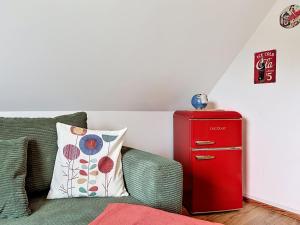 a red refrigerator next to a couch with a pillow at Apartment Eifelhome Two nahe Nürburgring by Interhome in Fuchshofen +21 photos