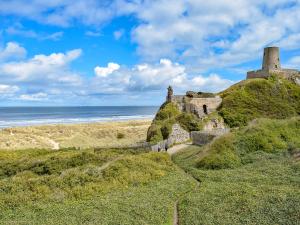 an old castle on a hill next to the ocean at The Caddy's Lodge - Uk47762 in Bamburgh