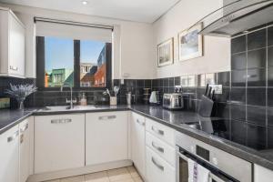 a kitchen with white cabinets and a black tiled wall at Windsor Castle Views - Spacious Flat - By Tempstay in Windsor