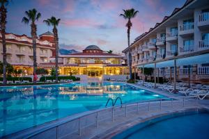 a hotel pool with palm trees and a building at Fun Sun Smart Lurea Beach in Kemer