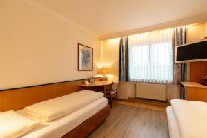 a hotel room with two beds and a desk at Parkhotel Crombach am Salingarten in Rosenheim