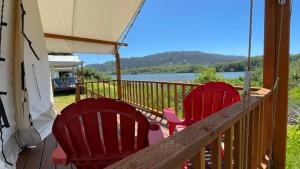 three red chairs on a porch with a view of a lake at Ruby Glamping tent - tent site #9 in Klamath