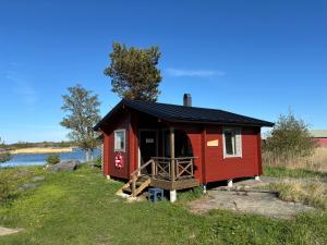 a red cabin with a black roof on a grass field at Klobbars Gästhem o Stugor in Kökar +13 photos