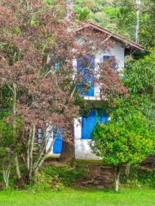 a white house with blue windows and trees at Chalé Refúgio Casarão in Passa Quatro
