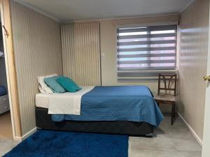 a bedroom with a bed with a blue blanket and a window at Caiquén Cabaña Punta Arenas in El Cerrillo