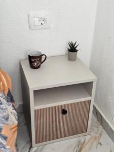 a white nightstand with a cup and a plant on it at Brita Apartman in Utjeha