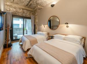two beds in a room with a mirror and a window at Sela V Hotel in Brooklyn