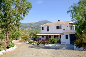 a white house with trees and mountains in the background at El Fresquedal in Alozaina