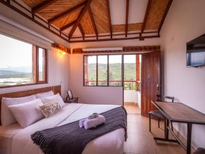 a bedroom with a bed and a desk and windows at Artemisa Hotel Villa de Leyva in Santa Sofía
