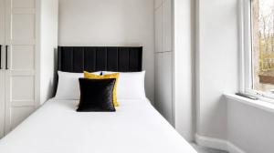 a white bed with a black headboard and yellow pillows at The Fountain View Apartment in Rothesay