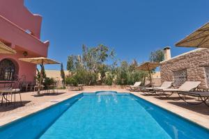 a pool with chairs and umbrellas next to a house at Villa Nouran - Chambre D'Hôte in Ghazoua