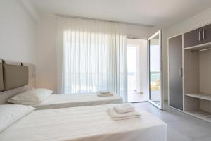 a white bedroom with two beds and a large window at Sumus Smart Residence in Porto SantʼElpidio